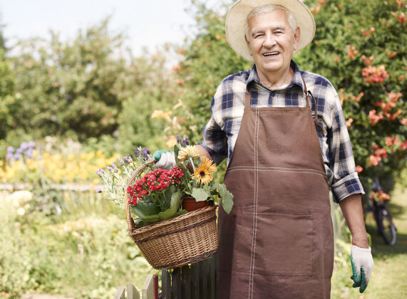 户外拿着花在地里干活的老人健康的生活方式老年人花园