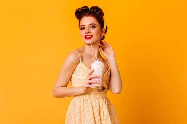 浪漫时尚的姜汁女孩喝奶昔摄影棚拍摄的黄色空间上孤立的女士时尚奶昔复制空间