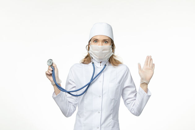 冠状病毒防护正面图女医生穿着医疗服戴口罩因冠状病毒手持听诊器对浅白壁病毒大流行冠状病毒-疾病到期病毒大流行