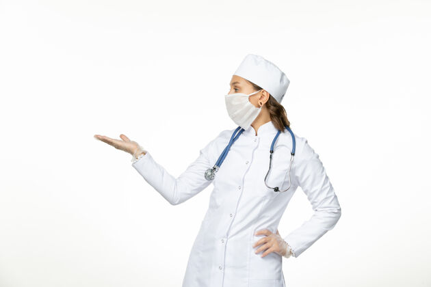 套装正面图女医生身穿白色医疗服戴口罩因冠状病毒对淡白色墙壁大流行性疾病隔离护士听诊器面罩