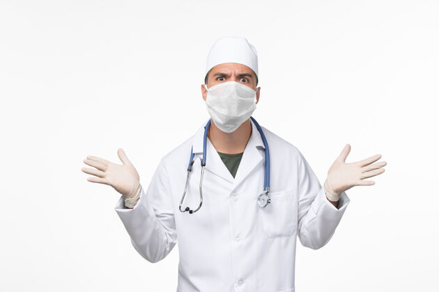 疾病正面图：男医生穿着医疗服 戴着口罩 戴着听诊器 在浅白的墙壁上看covid——疾病大流行视图套装疾病