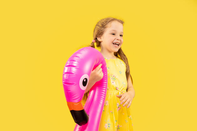 青少年美丽动情的小女孩被隔离在黄色的空间里半长的快乐孩子的肖像 穿着裙子 手里拿着橡皮粉色的火烈鸟金发童年小