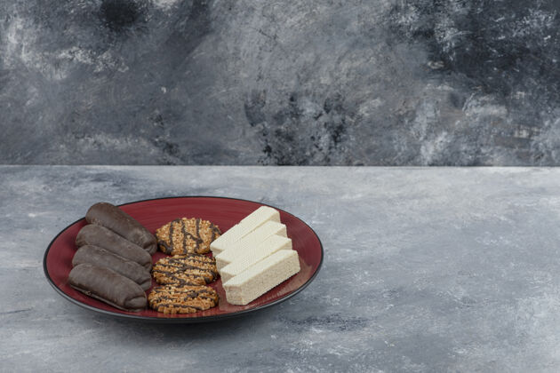 美味一个红色盘子 石头背景上放着燕麦片饼干和巧克力棒华夫饼燕麦片石头