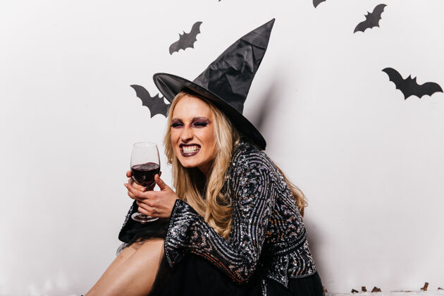 吸血鬼大笑的女巫喝着血戴着巫师帽的金发女孩在万圣节喝酒幽灵巫术神秘