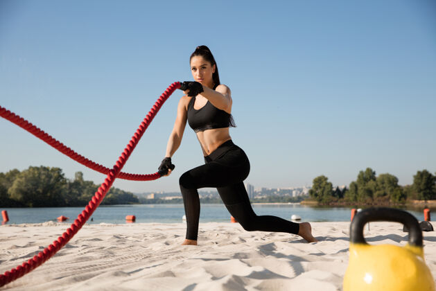 沙滩年轻健康的女人在沙滩上用绳子锻炼身体蹲健康锻炼