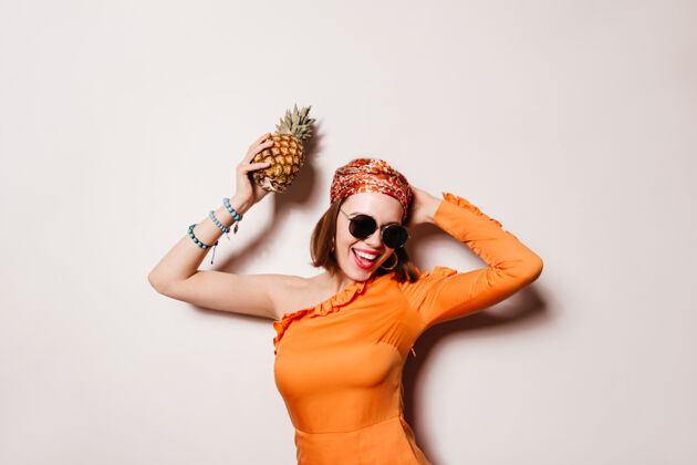 生命淘气的女孩穿着橙色的裙子 戴着太阳镜 胳膊上戴着蓝色的手镯 手里拿着菠萝跳舞头带好情绪