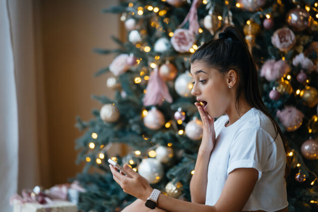 女人快乐的女人与家人或朋友视频通话年轻的女人在家里装饰好的圣诞树旁使用数字平板电脑震惊手机惊喜