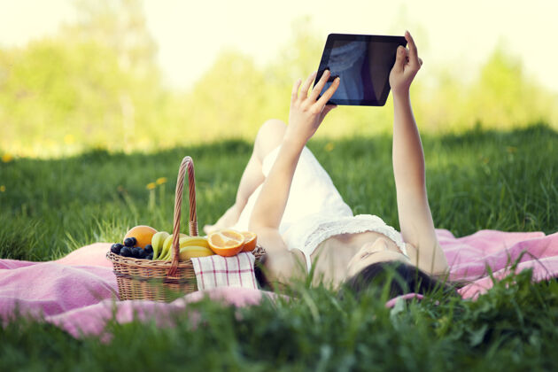 仰卧在草地上使用数字平板电脑的年轻女子数字平板电脑阳光互联网
