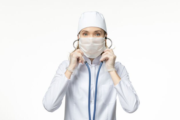 女性正面图女医生穿着白色医疗服 带无菌口罩 因冠状病毒使用听诊器对白墙疾病大流行性疾病冠状病毒-听诊器专业疾病