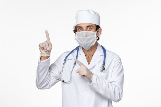 冠状病毒正面图身穿医疗服的男医生 戴着无菌口罩 以防感染冠状病毒-举起手指看白墙病毒大流行疾病医生病毒套装