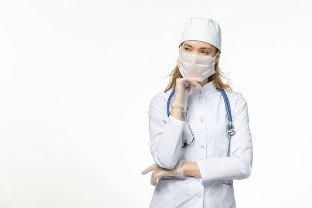 视图正面图女医生穿着医疗服戴着口罩和手套因冠状病毒思考白墙大流行冠状病毒病疾病正面护士