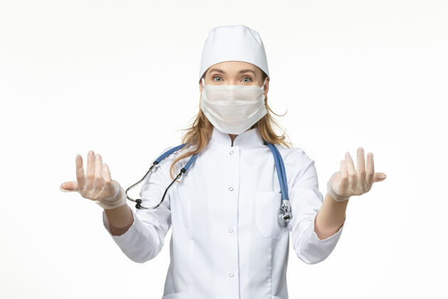 视图正面图女医生穿着医疗服 带着无菌口罩 由于白色办公桌上有冠状病毒疾病大流行健康病毒药品冠状病毒人员