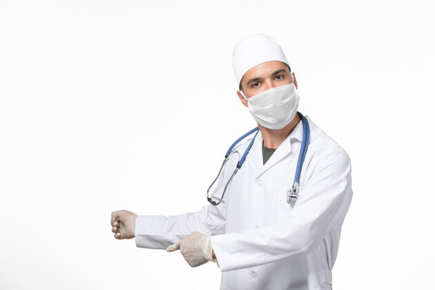 视图正面图男医生穿着医疗服 戴着口罩 因白墙上有冠状病毒-病毒大流行病毒病套装实验室外套外套