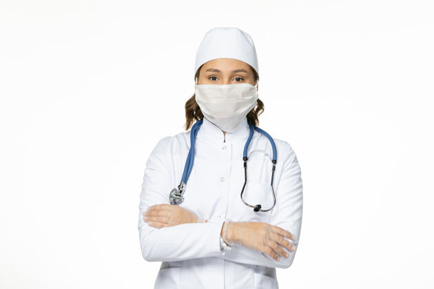 视图正面图女医生穿着白色医疗服戴口罩因冠状病毒在白墙上大流行病毒隔离前方护士居家