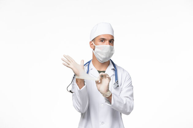 正面正面图：男医生穿着医疗服 戴着口罩 对抗白色墙壁上的冠状病毒病大流行病毒成人人人