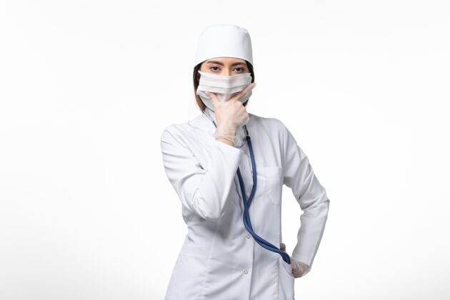 浅白色前视图女医生穿着白色医疗服 戴着口罩 因大流行于浅白墙上 医学大流行病毒covid-人女性人