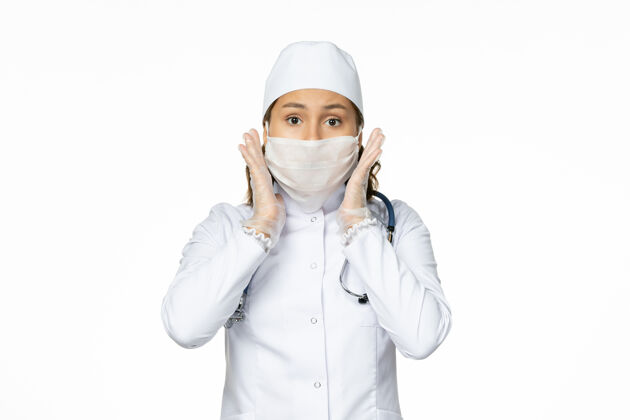 人正面图女医生身穿白色医疗服 戴口罩 因冠状病毒在淡白色墙壁上传播大流行性疾病隔离冠状病毒医学正面制服