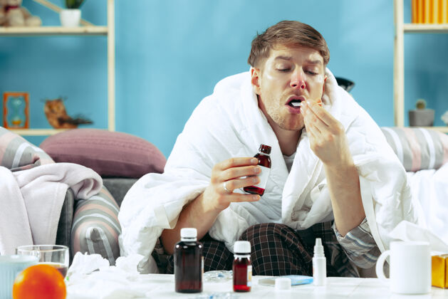支气管炎满脸胡须的病人 拿着烟道 坐在家里的沙发上 盖上温暖的毯子 喝着止咳糖浆对疾病 流感 疼痛有概念在家放松治疗疲劳发烧