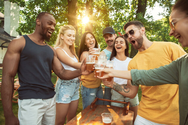 啤酒一群快乐的朋友在阳光明媚的日子里喝着啤酒 一起烧烤一起在户外的林间空地或后院休息餐食物自然