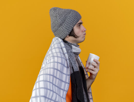 格子站在剖面图上的年轻病夫戴着冬天的帽子 围巾裹着格子呢 手里拿着一杯茶？风景冬天病