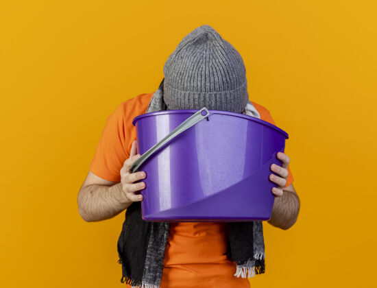年轻体弱多病的年轻人戴着冬天的帽子 戴着围巾 手里拿着塑料桶 往里面呕吐 把它隔离在橘子上帽子病橘子
