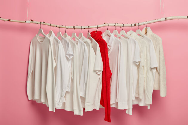 衬衫女士白色休闲装放在衣架上 红色针织保暖毛衣在整个系列中脱颖而出穿衣套装悬挂在粉色背景下家居衣柜经典风格时装店服装套头衫衣架