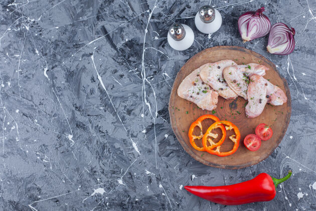 配料切好的甜椒 西红柿和鸡翅放在洋葱旁边的木板上 盐和胡椒放在蓝色的表面蛋白质营养板