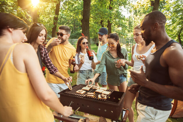 烧烤一群快乐的朋友在阳光明媚的日子里喝着啤酒 一起烧烤一起在户外的林间空地或后院休息花园啤酒餐