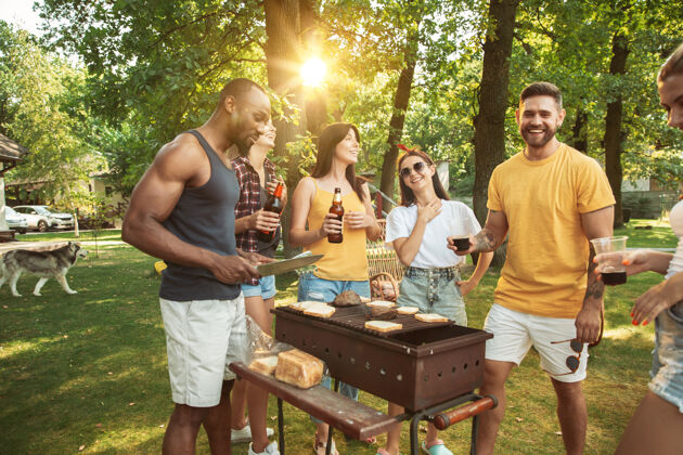 啤酒一群快乐的朋友在阳光明媚的日子里喝着啤酒 一起烧烤一起在户外的林间空地或后院休息啤酒食物朋友