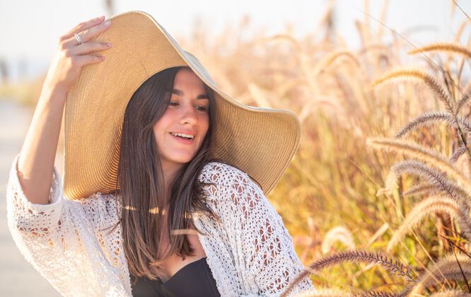 帽子一个快乐的女人在阳光下的肖像 坐在田野里 穿着夏装 戴着帽子波西米亚田野小穗