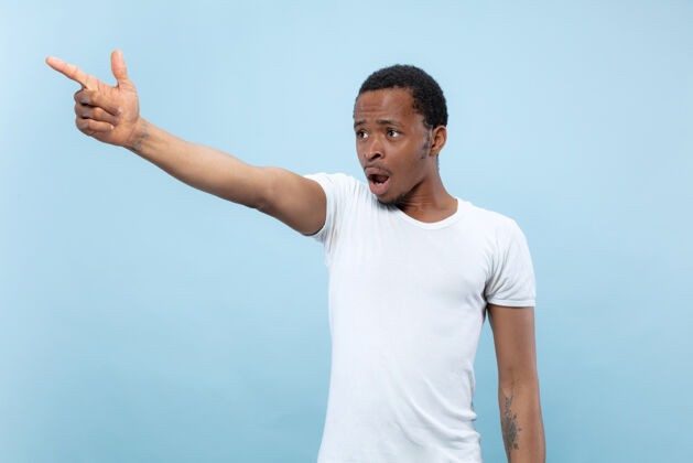 手势半身特写肖像的年轻非洲裔美国男子在白色衬衫的蓝色空间人类的情感 面部表情 广告 销售理念指向 选择 惊讶人类成功一半
