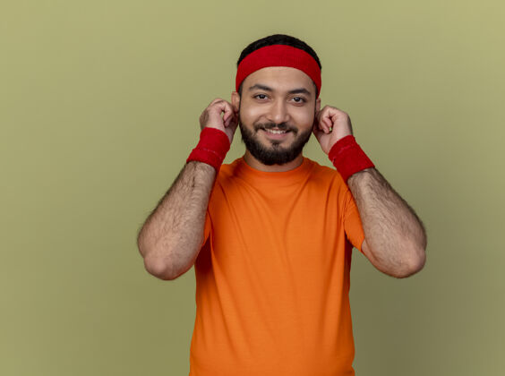 运动型微笑着的年轻人戴着头带和腕带 耳朵被隔离在橄榄绿上头带腕带微笑