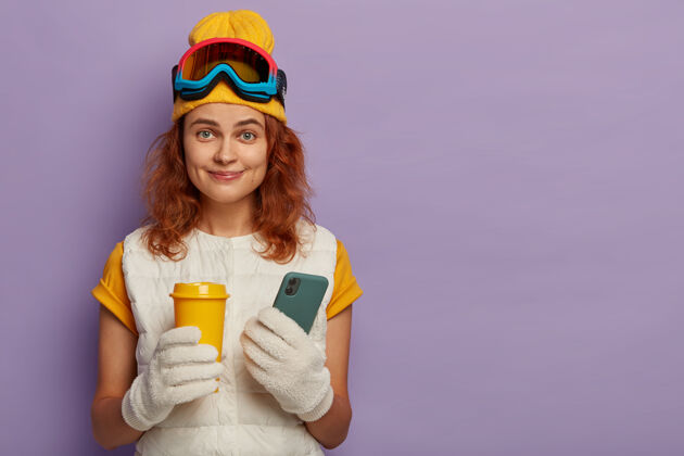 背心极限冬季运动 休闲和科技概念快乐的红发女人拿着外卖咖啡和现代手机 是一名职业滑雪者 在社交网络上发布照片立场生姜滑雪板