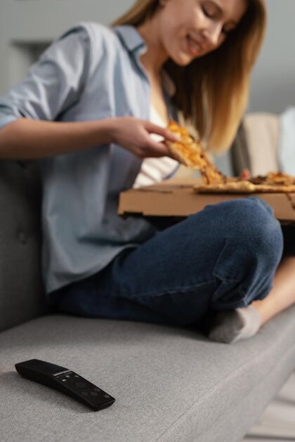 沙发女人边吃比萨饼边看电视特写披萨房子美味
