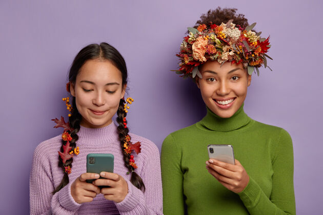 年轻照片中高兴的女性朋友手持现代智能手机 给朋友发信息 用创意的方式穿秋叶 有高兴的表情 穿毛衣一起毛衣表情