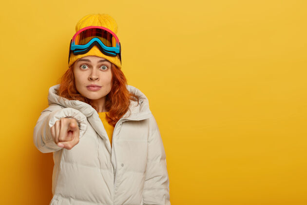 眼镜印象深刻的姜女滑雪点进入相机 穿着外套 滑雪护目镜 黄色背景隔离冬季度假概念惊喜一个极限