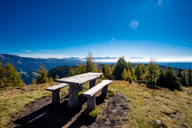 乡村木桌上有长凳 周围是意大利阿尔卑斯山 阳光下绿树成荫高山地标春天