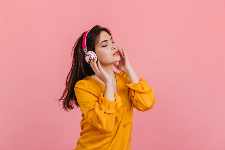 享受一个留着长发的女人 穿着鲜艳的衬衫 戴着白色和粉色的耳机 在隔离的墙上听音乐女孩梯子太阳镜