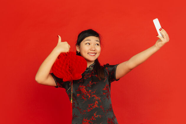 欢呼中国新年红色背景上孤立的亚洲少女肖像穿着传统服装的女模特看起来很开心 带着装饰自拍庆祝 节日 情感旗袍年普通话