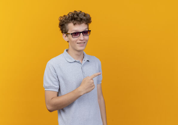 马球一个戴着黑眼镜 穿着灰色马球衫的年轻人愉快地笑着 用食指指着站在橙色墙上的一边手指欢呼男人