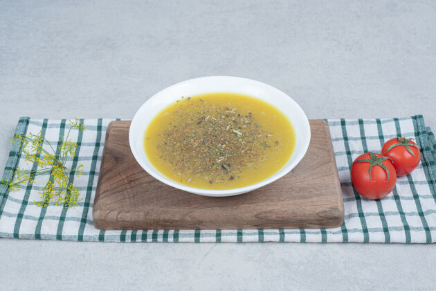 盘子美味的蔬菜汤和两个西红柿在桌布上胡椒板黄