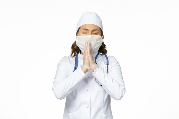 医生正面图年轻女医生戴着无菌口罩和手套因冠状病毒在白色表面祈祷祈祷口罩冠状病毒