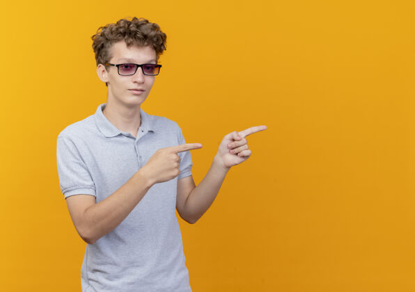 男人一个戴着黑眼镜的年轻人 穿着灰色马球衫 脸上带着微笑 手指着站在橘色墙上的一边看指指点点壁板