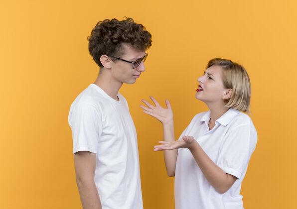 夫妻一对年轻的运动情侣站在橘色的墙上看着彼此争吵在一起看运动