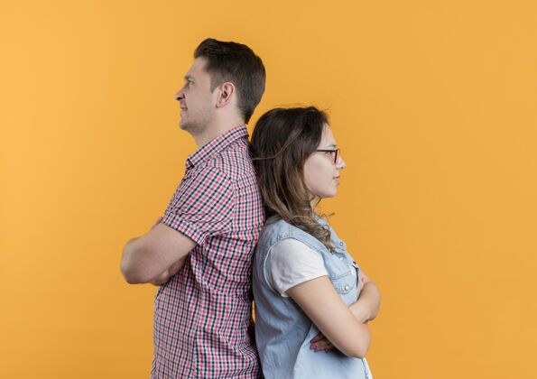 打架一对穿着休闲服的年轻夫妇站在橘红色的墙上 背靠背地站在一起衣服之后男人