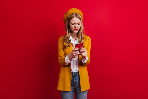 金发专注的法国女孩发短信穿着休闲服的金发女郎在红墙上用智能手机优雅年轻夹克