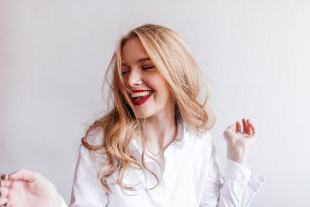 无忧无虑穿着白衬衫的快乐的欧洲女人表达积极的情绪光明墙上快乐的金发女孩年轻人年轻情感