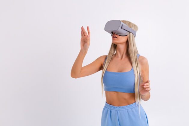 现实摄影棚照片中一个年轻迷人的女子穿着温暖的蓝色时尚西装 戴着虚拟现实眼镜在白色的科技游戏女性