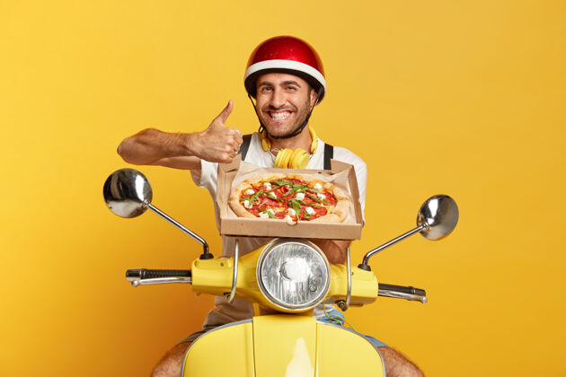 男性快乐的送货员戴着头盔开着黄色踏板车 手里拿着披萨盒头盔微笑骑手