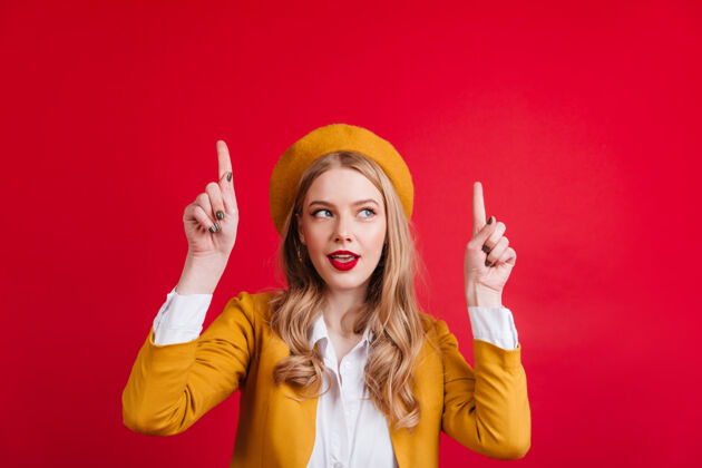 乐观一位穿着黄色贝雷帽 手指向上的白人女士一位可爱的法国女孩在红墙上做手势年轻手势表情
